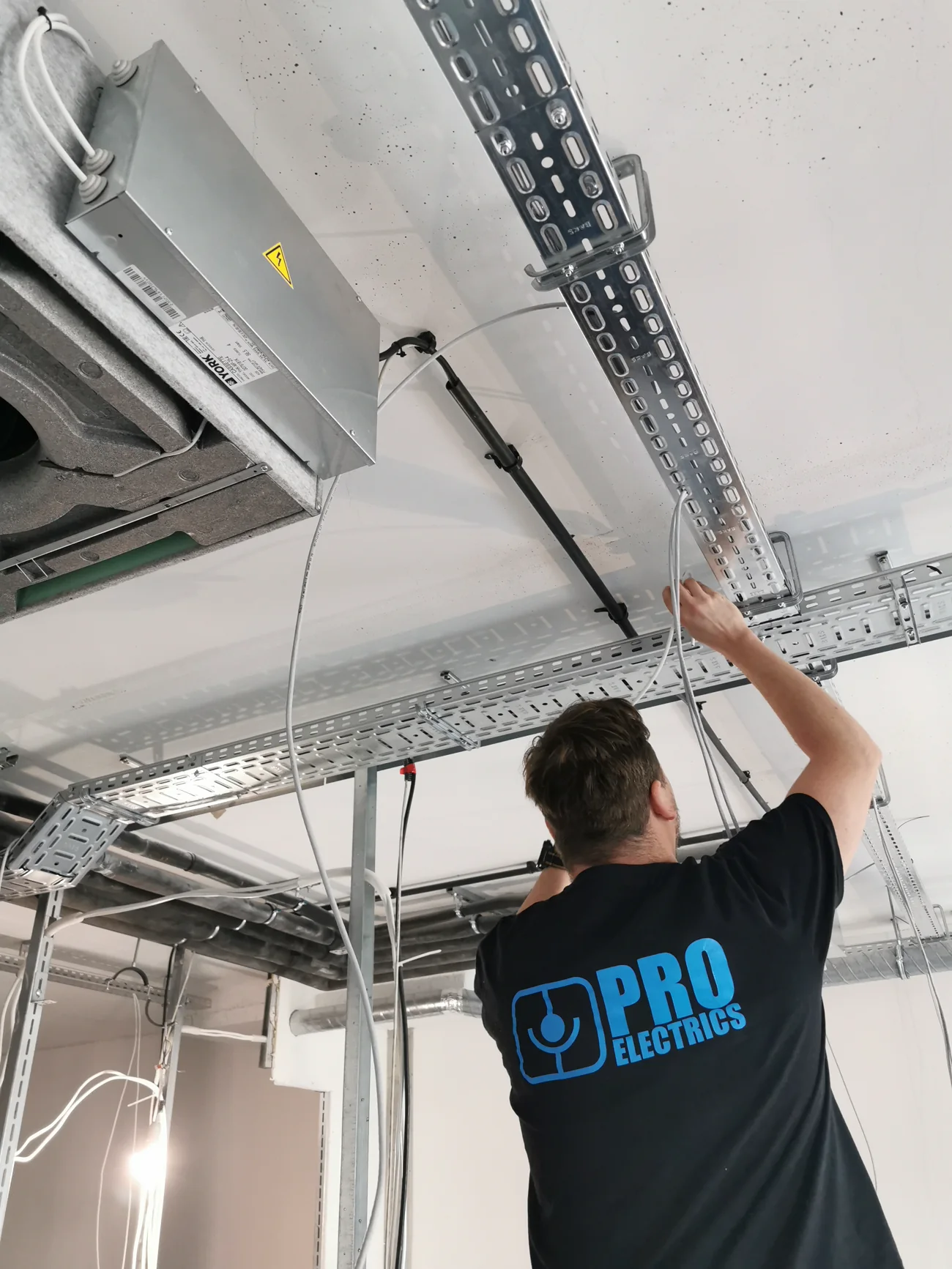 Technik PROelectrics prowadzi przewód w korytkach BAKS pod stropem obiektu